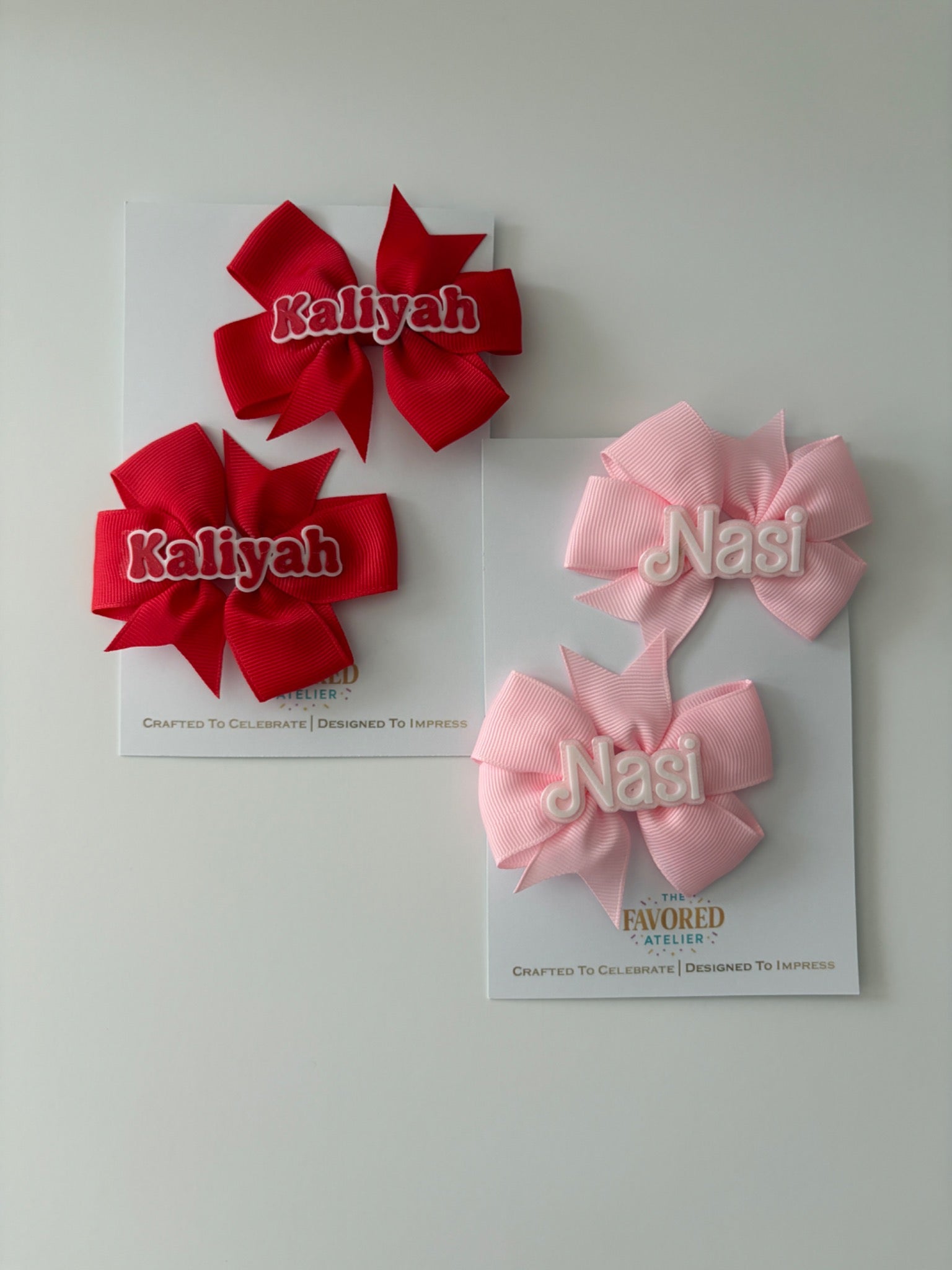 Personalized red and pink 3D name hair bow pairs on The Favored Atelier display cards
