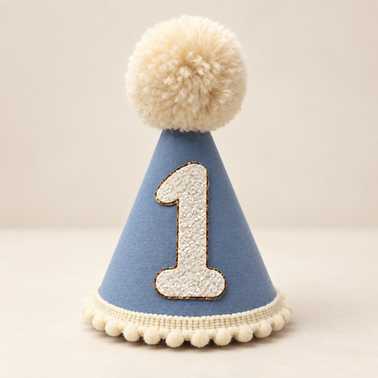 Blue first birthday party hat with cream pom pom and white glitter number one